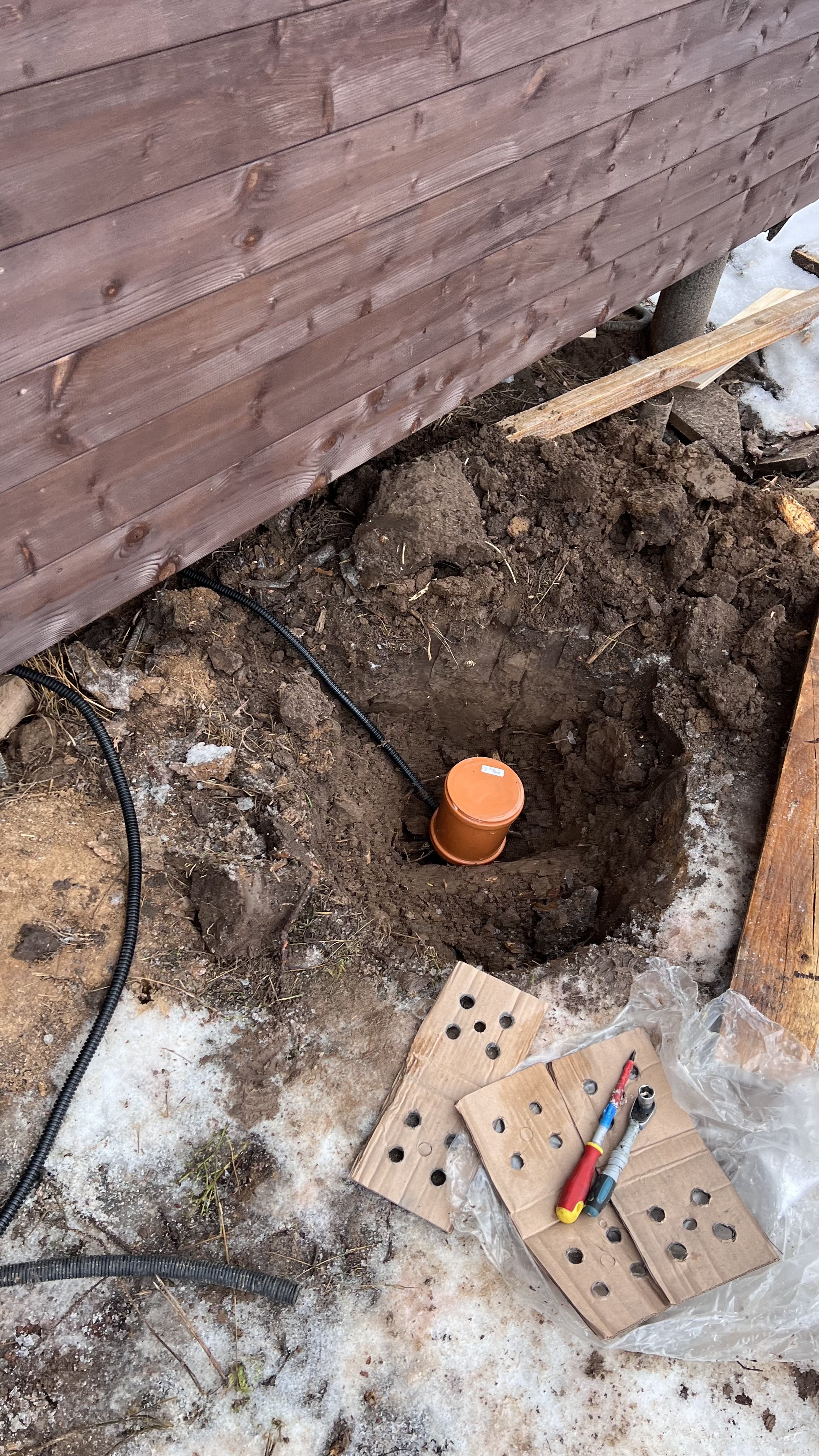 Заземление в частном доме: пластиковый корпус в выкопанной яме, рядом инструменты и доски.
